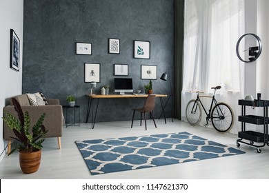 Patterned Carpet In Bright Workspace Interior With Bicycle Next To Brown Chair At Desk. Real Photo