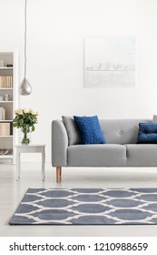 Patterned carpet in front of grey couch with blue pillows in white loft interior with flowers. Real photo