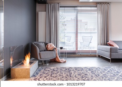 Patterned carpet and grey armchair with pink blanket near fireplace in contemporary apartment interior