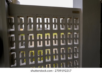 A patterned concrete wall with rectangular cutouts shows an outdoor yard view behind it in daylight.