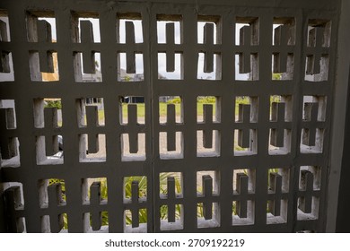 A patterned concrete wall with rectangular cutouts shows an outdoor yard view behind it in daylight.