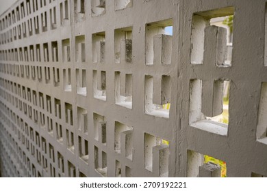 A patterned concrete wall with rectangular cutouts shows an outdoor yard view behind it in daylight.