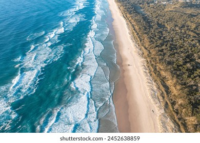 Patterned foamy ocean waves roll in and approach sandy beach. Majesty turquoise sea. Top view drone