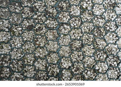 Patterned ground surface with interlocking grid filled with gravel and soil, used for permeable paving or eco-friendly walkways.