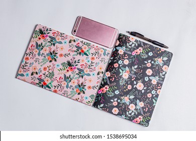 Patterned notebooks on white backdrop. Flower pattern on paper notebooks. Pink and black fancy girly things. Teenage girly pinky diary. Pink phone on white surface. Flower botanical pattern. Cute note