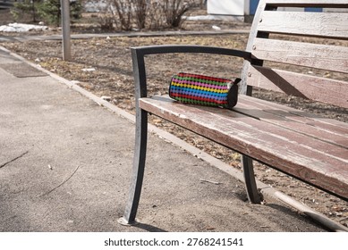Patterned pencil case with raised dot texture and zipper left on a worn wooden bench, indicating a misplaced school item during daily outdoor activity