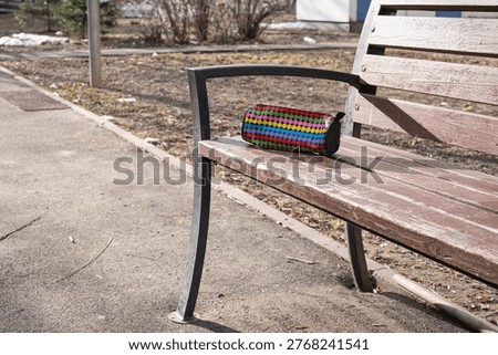 Patterned pencil case with raised dot texture and zipper left on a worn wooden bench, indicating a misplaced school item during daily outdoor activity