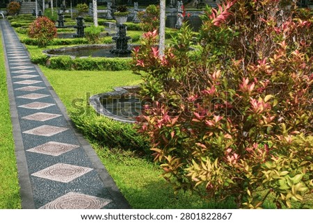 Patterned stone pathway through manicured gardens with ponds and shrubs at Tirta Gangga water palace, Karangasem, East Bali, Indonesia.