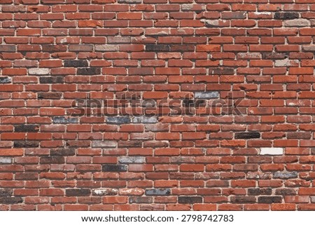 A patterned texture of an aged brick wall with bricks in various shades of red and some white bricks of an outdoor building on a sunny day