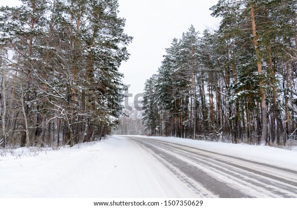 Patterns on the winter highway in the form of\
four straight lines. Snowy road on the background of snow-covered\
forest. Winter\
landscape.