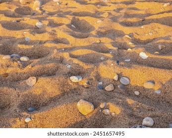 The patterns of pebbles and sand on the beach at sunset create mesmerizing natural artwork. The skys hues reflecting on the wet sand add to the beauty, making it a serene moment to behold.