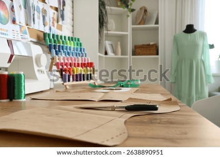 Patterns with sewing machine and thread spools on tailor's table in atelier, closeup