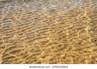 Patterns of the sun shining through the crystal clear  water and the sand wave formations with scattered white rocks near the shore of the Mediterranean Sea in Israel.
