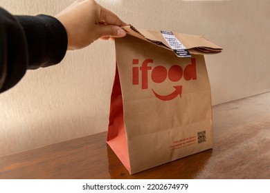 São Paulo, Brazil. August 20, 2022. Hand Picking Up Ifood Delivery Bag On Wooden Table.