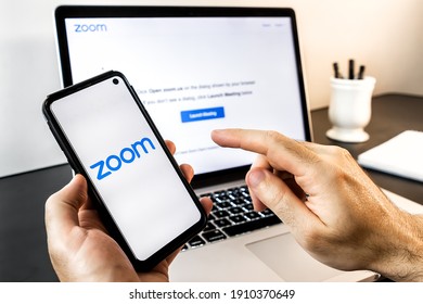 São Paulo, Brazil - February 2021: Hands Holding A Mobile Smart Phone Device Showing Zoom Video Communications Inc. App Logo On Screen And A Notebook Showing The Login Page For A Video Conference Call