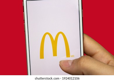 São Paulo, Brazil. February 24, 2021.
McDonald's mobile app - Hand holding a white cell phone on a red background. Selective focus. 