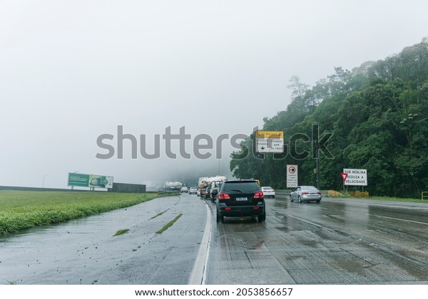 São Paulo, Brazil -\
September 30, 2021: Under fog, slow down. Imigrantes highway:\
Intense traffic with rain and fog. A billboard asks you to respect\
speed limits.