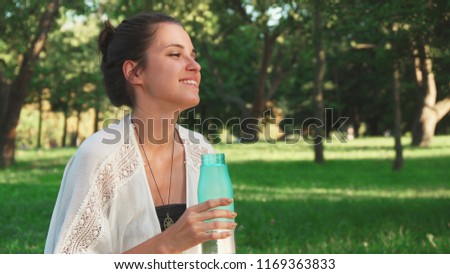 In the pause between the yoga classes beautiful girl is drinking water. She feels hapiness and smile