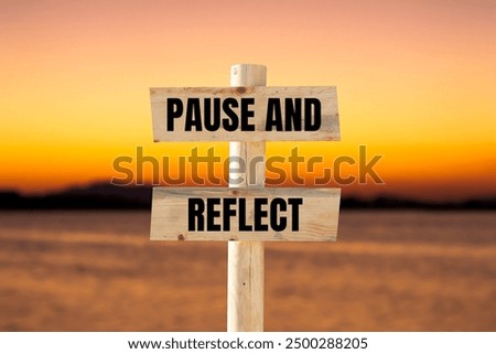 Pause and reflect message written on wooden sign with blurry lake background. Conceptual pause and reflect symbol. Copy space.