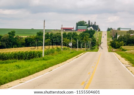 Paved hilly road with two distant cars going in opposite directions across farm country on a cloudy summer morning in northern Illinois, USA, for rural, agricultural, and travel themes