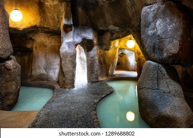 Paved path in a cave with water. Light at the end of the tunnel. Yellow lights illuminate the grotto.