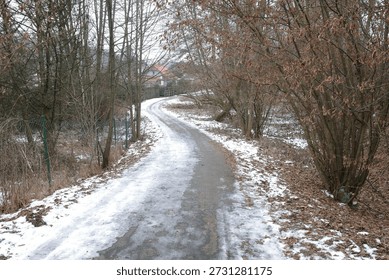 A paved path curves through a wintry landscape. Bare trees line the route, their branches devoid of foliage. Snow covers the ground alongside the path - Plzen, Czech - Jan,25,2026