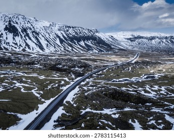 Paved road cutting through a dramatic winter volcanic landscape under a cloudy sky