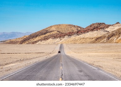 A paved road or highway in the sunny desert leading to the horizon, Death Valley National Park, California, USA