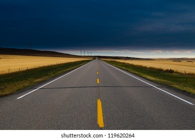 Paved Road Through Alberta Farmlands With Windmills At Dawn