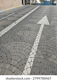 Paved street with cobblestone pattern and white directional arrow