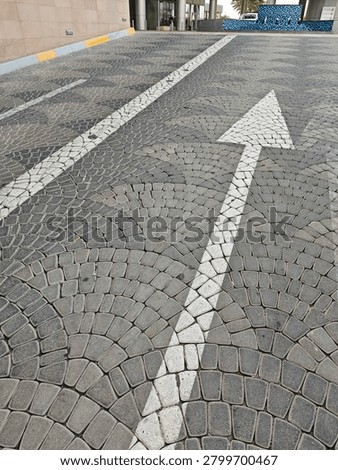 Paved street with cobblestone pattern and white directional arrow