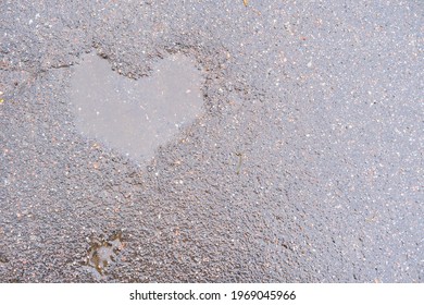 pavement after rain with a puddle in a shape of heart. wet dark grey road with flaws in a form of a heart filled with water, space for text, seeing love everywhere, natural imperfection of roads