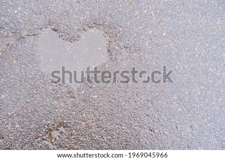 pavement after rain with a puddle in a shape of heart. wet dark grey road with flaws in a form of a heart filled with water, space for text, seeing love everywhere, natural imperfection of roads
