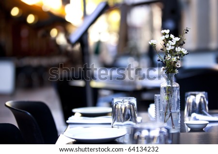 Pavement cafe table, with casual setting.  Focus on flowers, with blurred background.