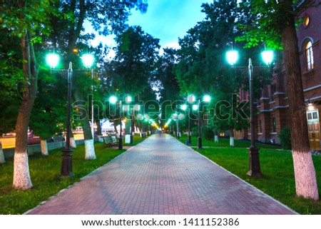 Pavement walkway at night in the green light of symmetrically lampposts, leading to the center of the frame. Pushkin street near the Opera and Ballet Theater, Ufa, Bashkortostan, Russia.
