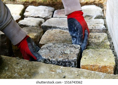 pavement works, Cobbled pavement natural stone. gloved Hands of worker installing concrete paver blocks. Hands of a bricklayer laying paving stones carefully placing, building a ramp way in garden
