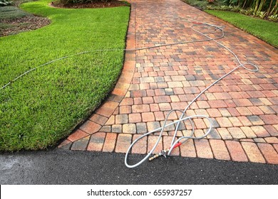 Paver driveway professionally pressure cleaned, with the hose and wand on the driveway. 