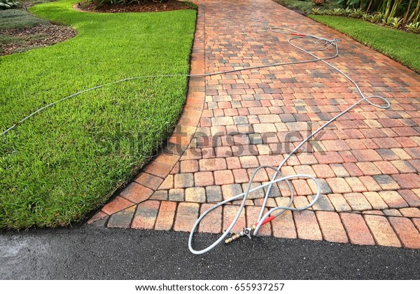 Paver driveway professionally pressure\
cleaned, with the hose and wand on the driveway.\
