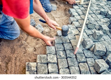 paving pavement with granite stones, workers using industrial cobblestones for paving terrace, road or sidewalk