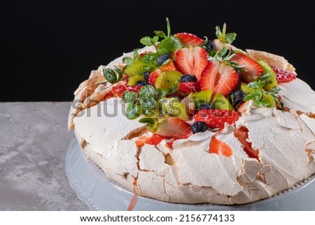 Pavlova cake with cream and fresh summer berries and kiwi on wooden background. Close up of Pavlova dessert with forest fruit and mint. Food photography