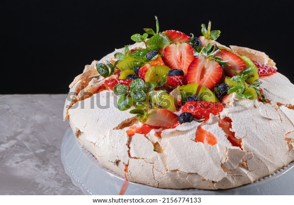 Pavlova cake with cream and fresh summer\
berries and kiwi on wooden background. Close up of Pavlova dessert\
with forest fruit and mint. Food\
photography