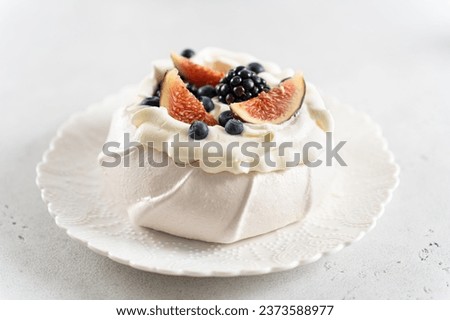 Pavlova cake with meringue, whipped cream, fresh blueberry, figs and blackberry on white background. Close up. Summer meringue dessert recipe, menu. Confectionery, cooking book