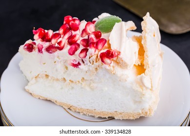 Pavlova cake with pomegranate and fresh mint leaves on white plate