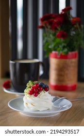 Pavlova Dessert With Berries And A Cup Of Coffee By The Window. Morning Breakfast In A Cafe With A Delicate Dessert With Cheese Cream And Fresh Berries By The Cafe Window.