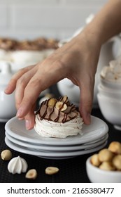 Pavlova dessert with chocolate and hazelnuts in hand. There is a dessert and white dishes on the table, a light background. Cream with mascarpone and whipped cream.