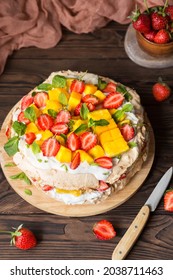 Pavlova with strawberries, mango and coconut cream. Cakes made of cane sugar. Tropical cake. Exotic dessert with mint. Strawberries on a wooden table. New Zealand food