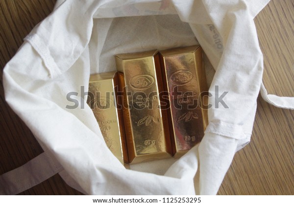 Pavlovsky Posad, Moscow region / Russia\
- August 24, 2016 - Three packs of chocolate in golden cover\
looking like golden bullions in an open canvas white\
bag