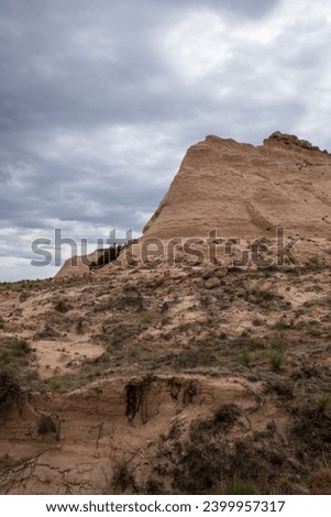 Pawnee Buttes in the northeastern portion of Colorado.  Arid and dry, desert scrub and rocky outcroppings. Cloudy sky, tan rock and subdued green scrub bushes.
