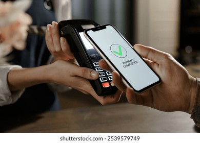 Pay by cell-phone on electronic payment machine or card reader. E-money at cashless wallet of client. Male with and cellphone and female hands with POS-terminal at store close-up. Buying food order