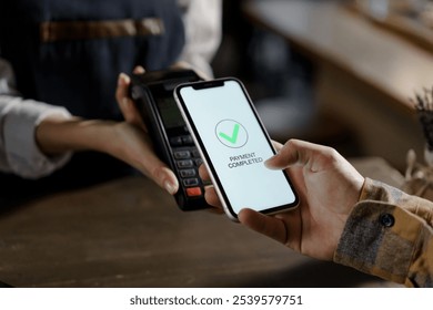 Pay by cell-phone on electronic payment machine or card reader. E-money at cashless wallet of client. Male with and cellphone and female hands with POS-terminal at store close-up. Buying food order